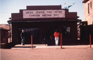 People standing outside United States Post Office Cameron Arizona; dirt street, red posts (for parking?)